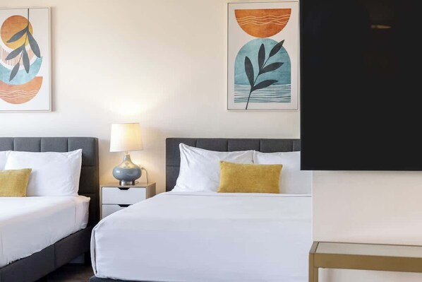 A hotel room with two beds, a nightstand with a lamp, and abstract artwork on the walls.