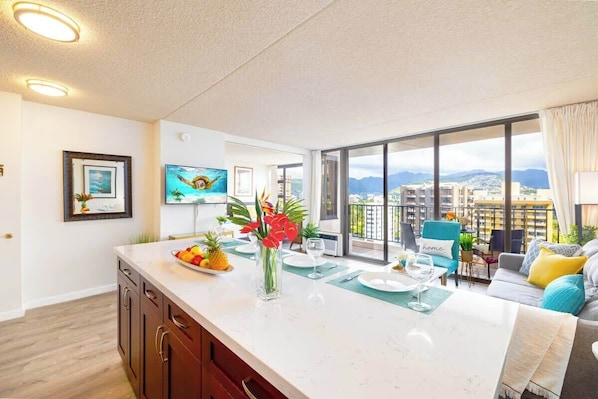 A modern kitchen with a large island, dining area with a view, and a balcony with a cityscape.