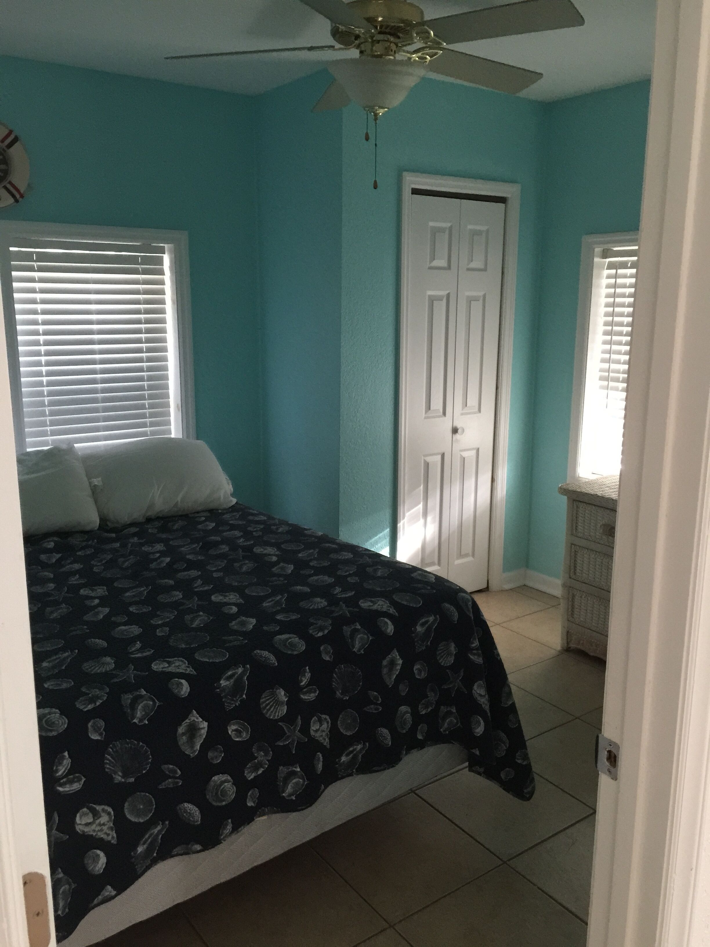 A bedroom with a bed, a ceiling fan, a door, and a window with blinds.