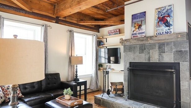 A cozy living room with a fireplace, a black leather sofa, and a television mounted above it. - 2 Bed Exceptional Fireplace Condo In the Heart of Town On Shuttle Route (Ludlow)