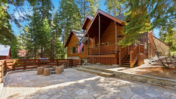 A log cabin with a stone patio and a wooden deck.
