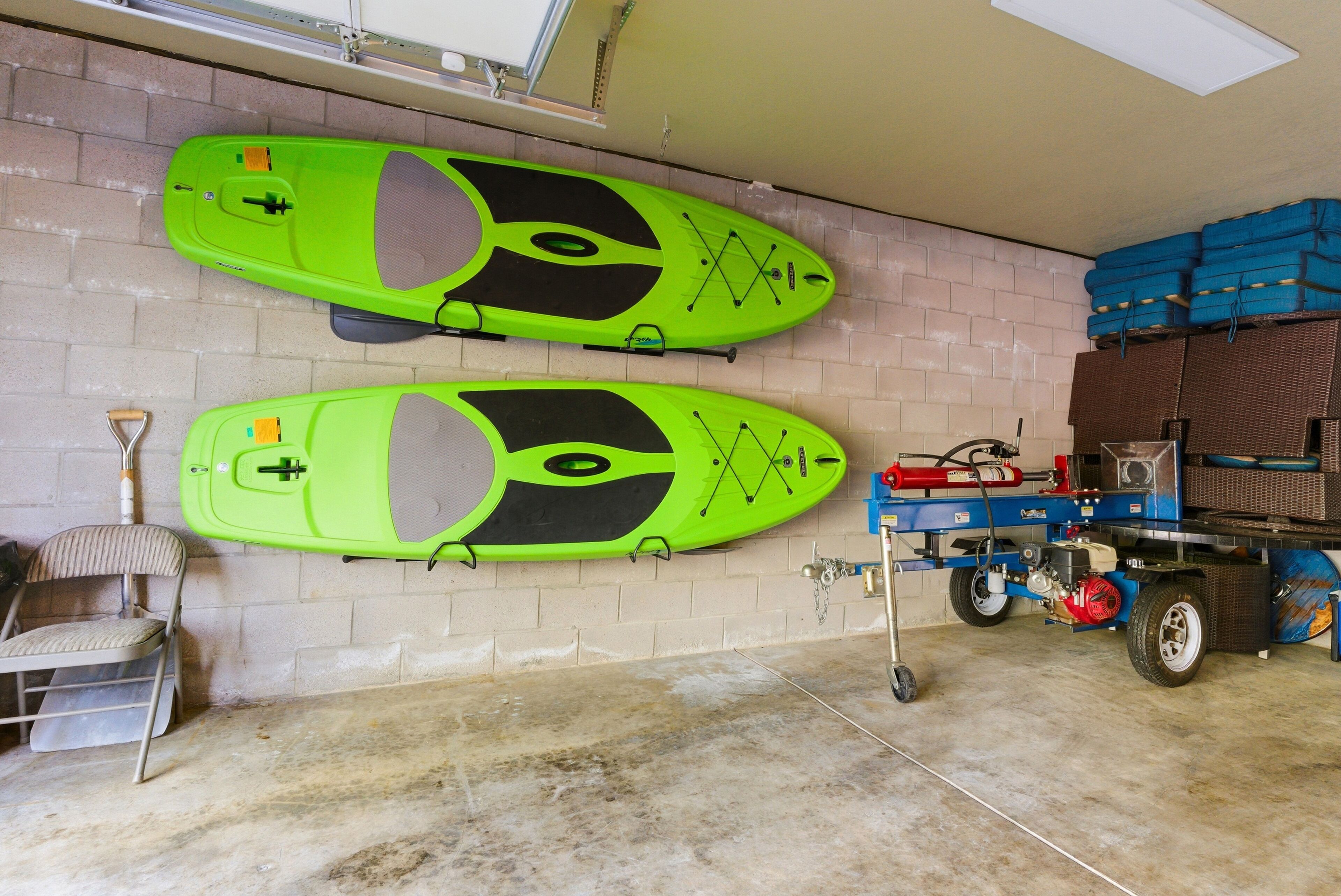 Due kayak montati su una parete in un garage, con una sedia, un estintore e un carrello portaoggetti blu.