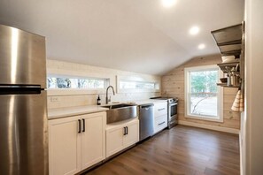 A modern kitchen with white cabinets, stainless steel appliances, and a wooden floor.