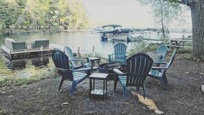 Järvenrantainen oleskelualue, jossa on Adirondack-tyylisiä tuoleja ja pieni pöytä. Alue on puistomaisesti maisemoitu, ja sitä ympäröivät puut sekä laituri.