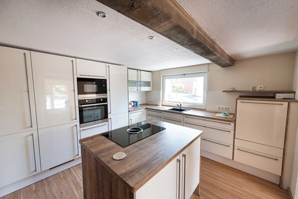 A modern kitchen with white cabinetry, a built-in oven, a microwave, and a wooden island with a sink.