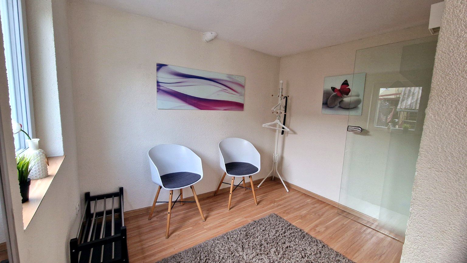 Una habitación con dos sillas blancas, un tapete, un cuadro y un vidrio.