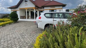 A two-story building with a red-tiled roof, a covered porch, and a paved driveway. - Virunga House (Muhoza)