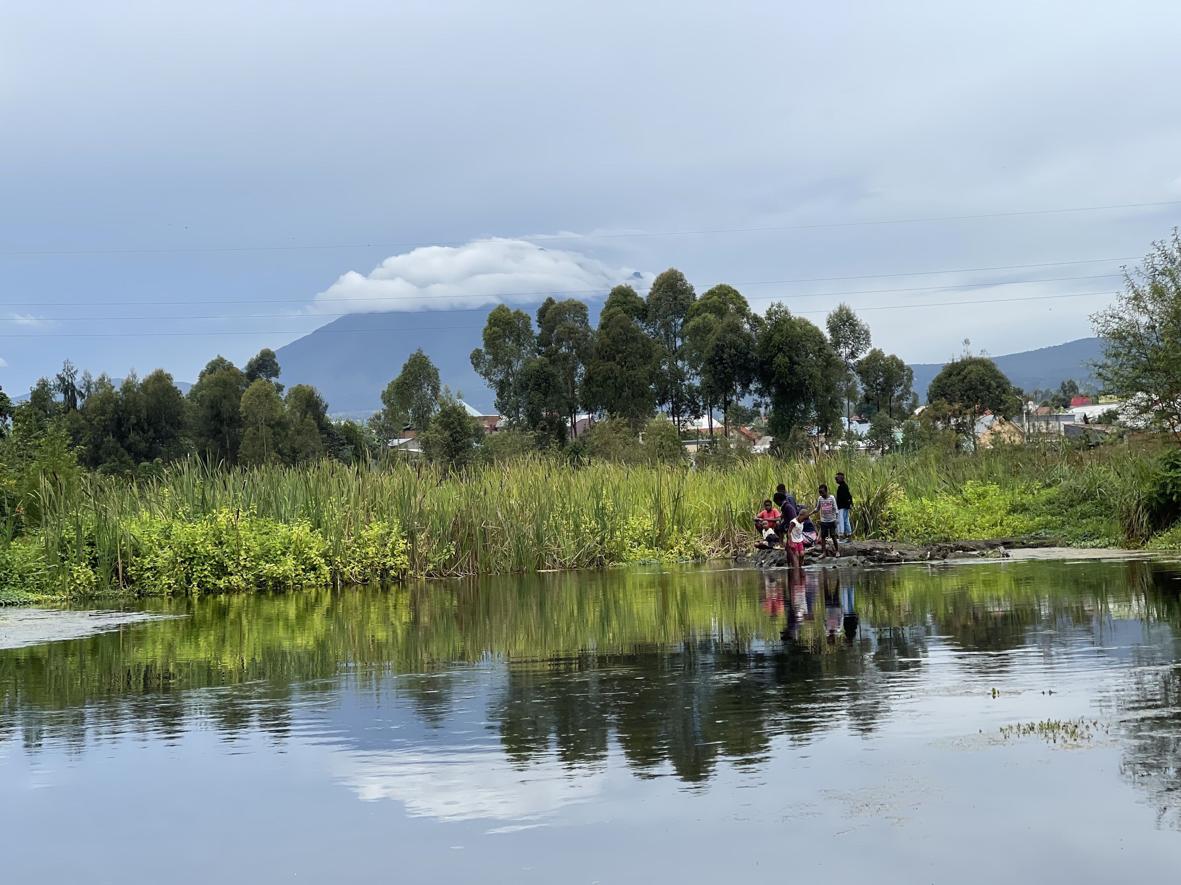 Un río tranquilo con gente cerca de la orilla, rodeado de abundante vegetación y árboles.