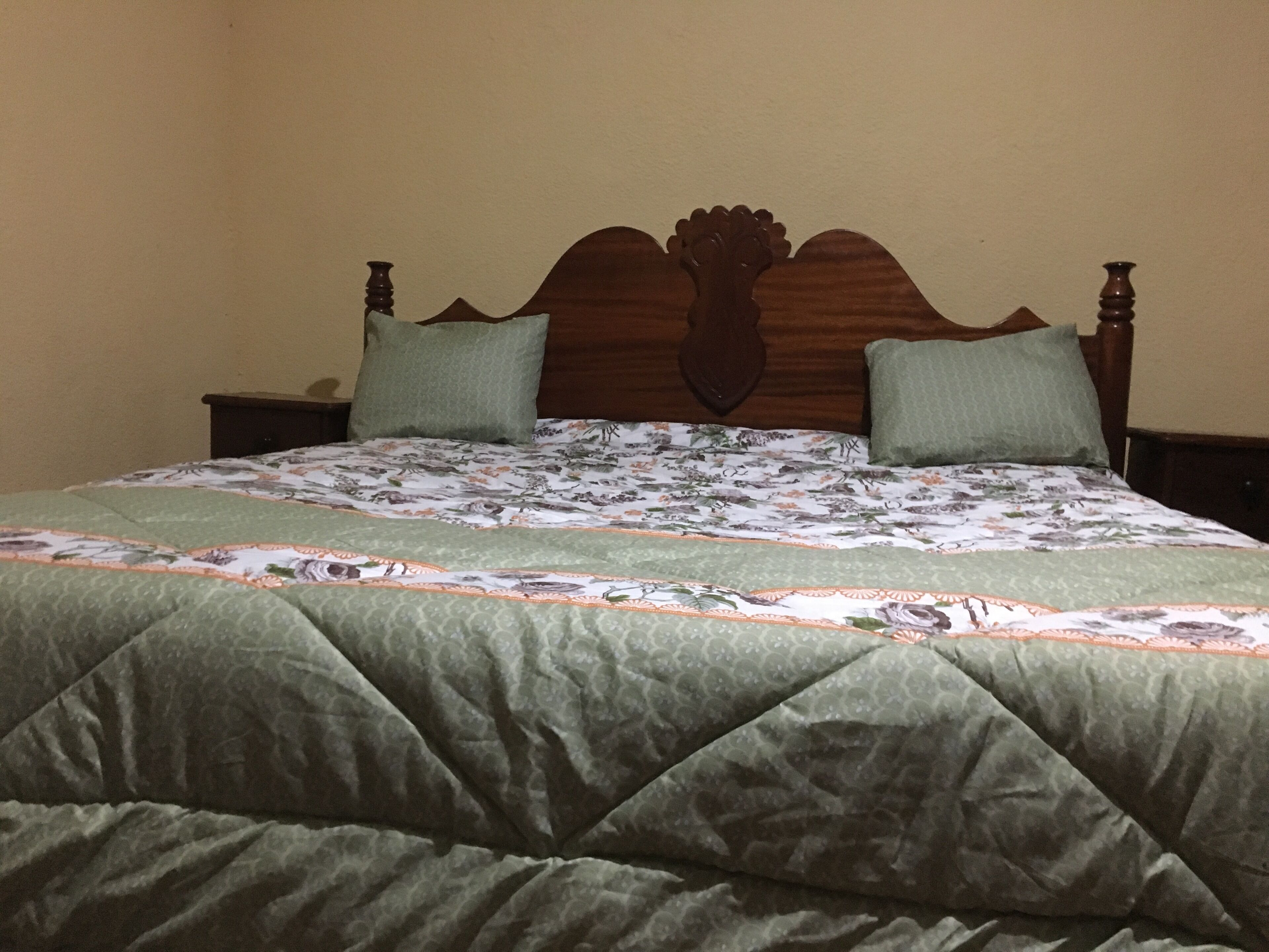 A bed with a floral bedspread, two pillows, and a wooden headboard.