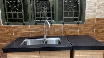 A kitchen with a black countertop, stainless steel sink, wooden cabinets, and decorative window grills.