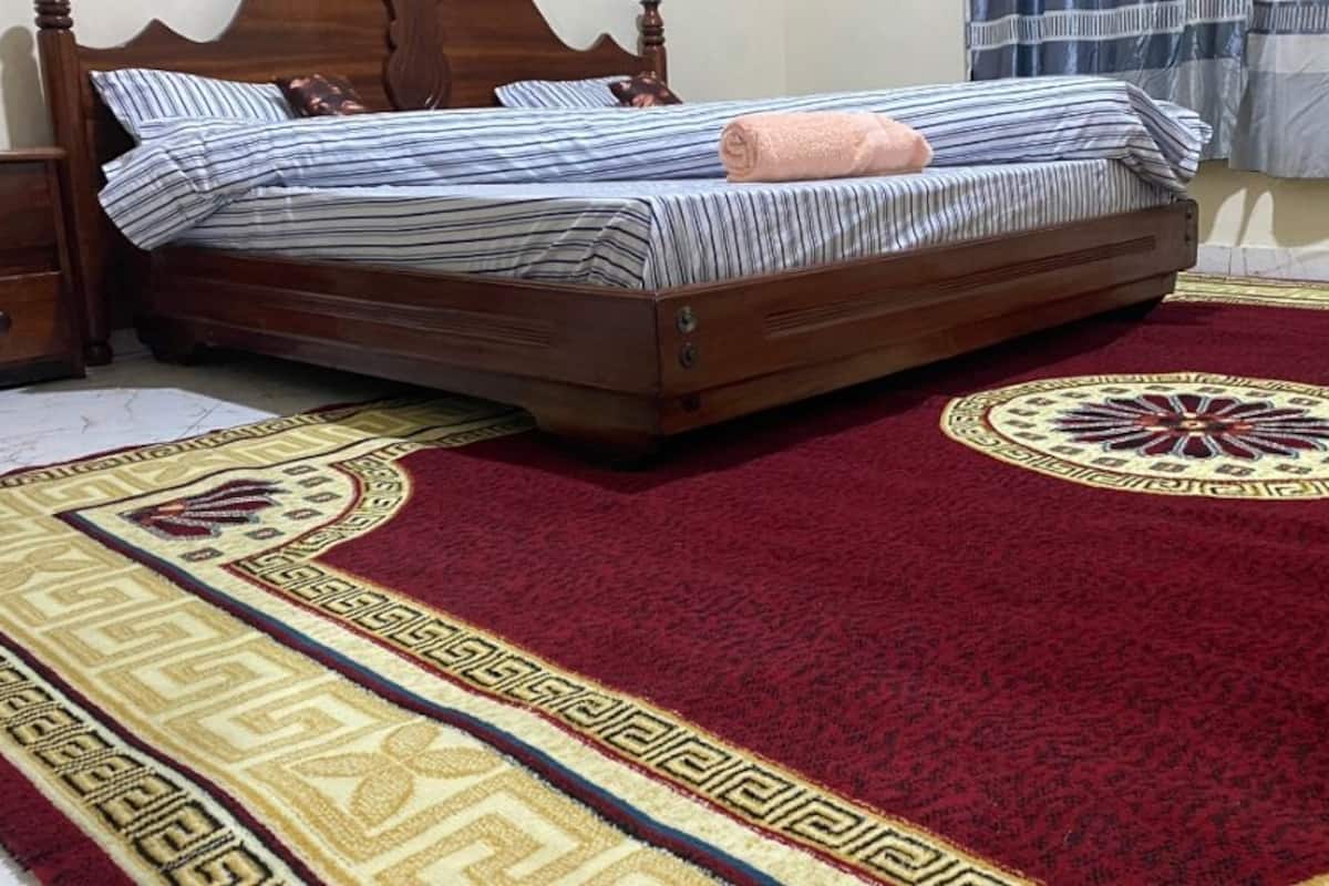 A bedroom with a wooden bed, a nightstand, a patterned rug, and a window with curtains.