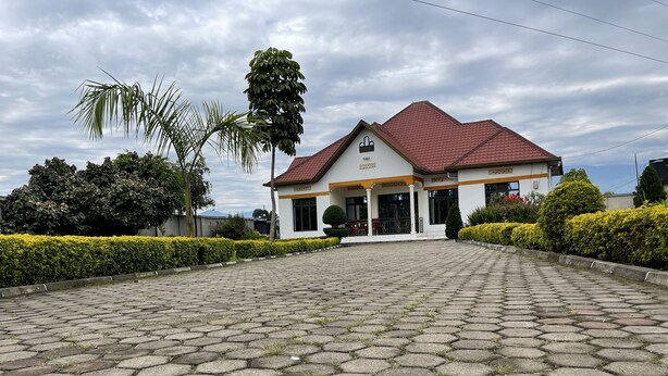 A building with a red-tiled roof, a white facade, and a paved entrance area. - Virunga House (Muhoza)