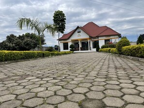 A building with a red-tiled roof, a white facade, and a paved entrance area. - Virunga House (Muhoza)
