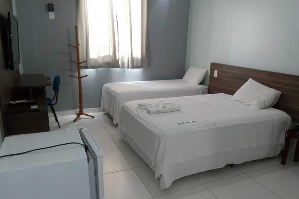 Una habitación de hotel con dos camas, un escritorio con computadora, una silla y un perchero.
