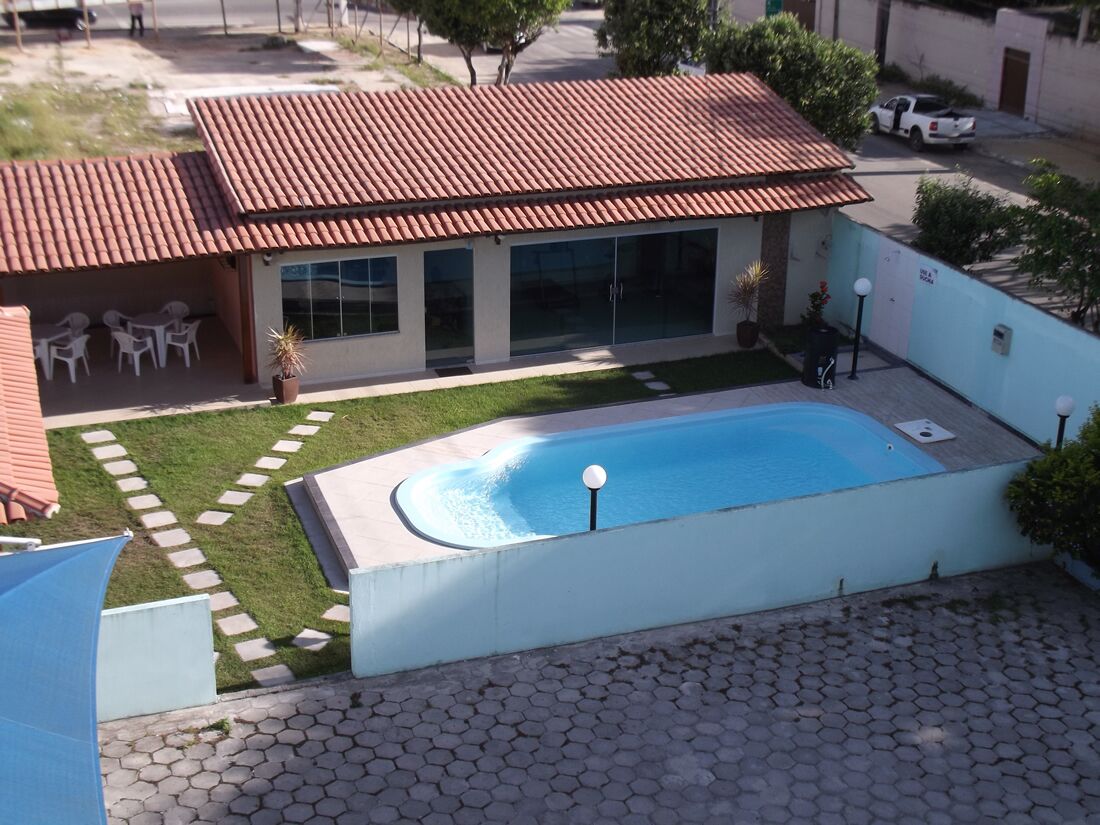 Ein Wohnhaus mit Swimmingpool, einer überdachten Terrasse mit Sitzgelegenheiten und einem kleinen Garten.