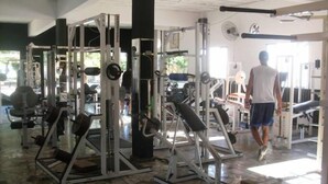 A gym with various exercise machines, a person walking, and a stone-tiled floor. - Hotel Jacarandá (Teixeira de Freitas)