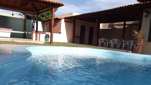 A swimming pool with a tiled deck, surrounded by covered seating areas and a building with a tiled roof. - Hotel Jacarandá (Teixeira de Freitas)