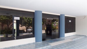 A building entrance with a security camera area, blue pillars, and a tiled floor. - Hotel Jacarandá (Teixeira de Freitas)