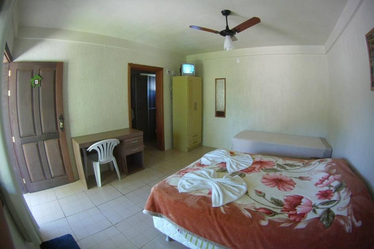 A bedroom with a bed, a desk, a chair, a wardrobe, and a ceiling fan.