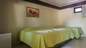 A room with a bed covered in green sheets, a small table with a tablecloth, a radiator, and a painting on the wall. - Pousada dos Plátanos (Nova Petropolis)