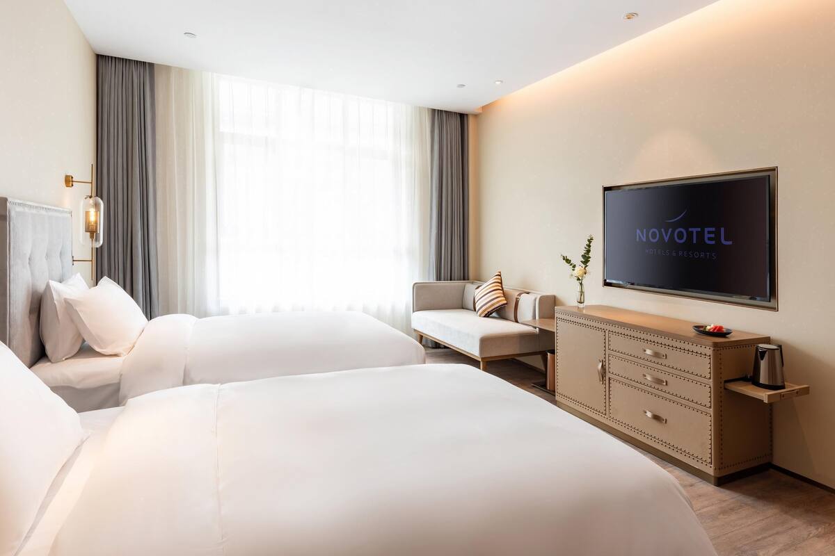 A hotel room with two beds, a sofa, a TV, and a minibar.