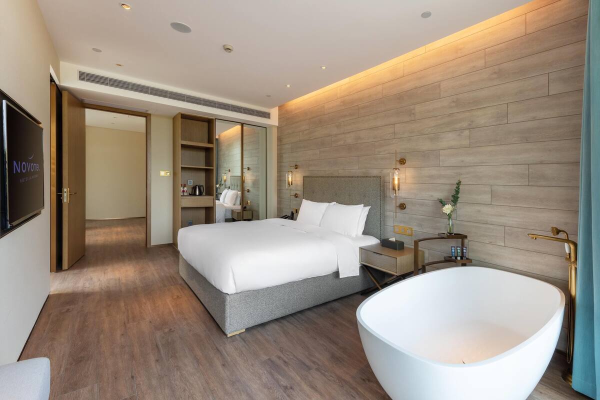 A modern hotel room with a large bed, a freestanding bathtub, and a walk-in closet.