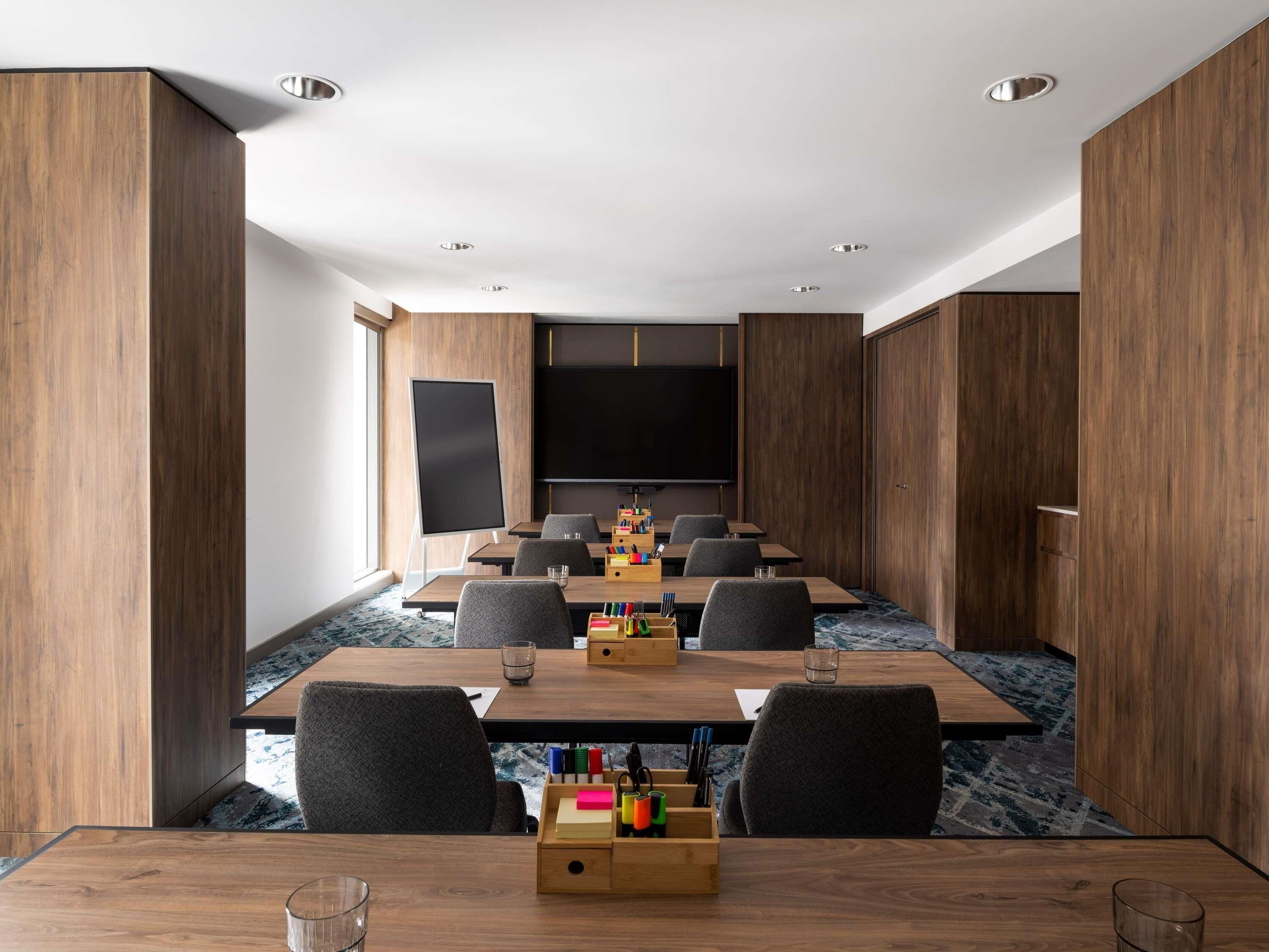 A conference room with a large table, chairs, a projector screen, and a TV.