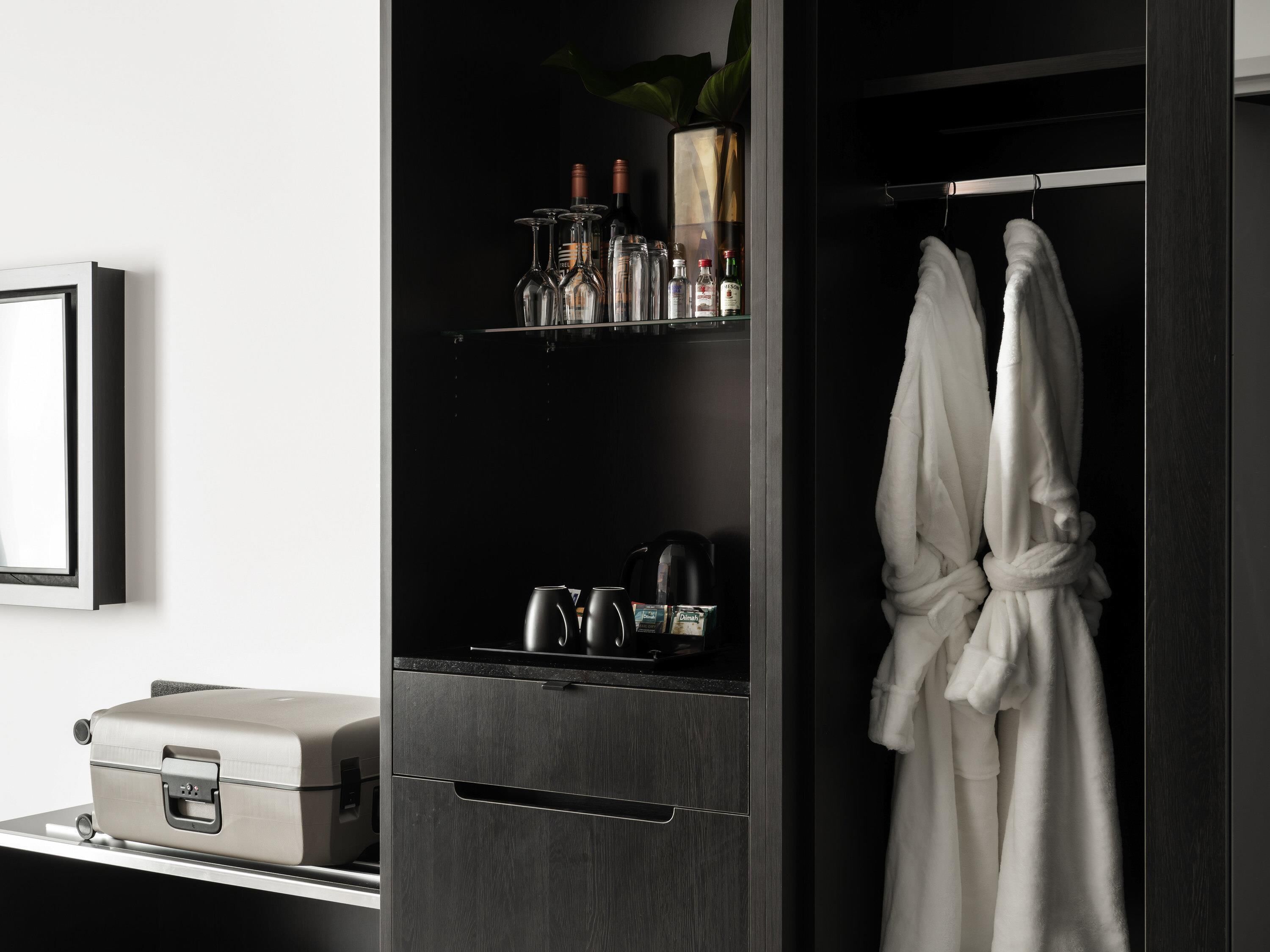 Un baño moderno con tocador de madera oscura, un perchero con bata blanca y un estante con botellas y una cafetera.