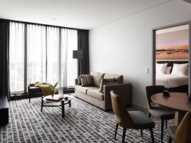 Une chambre d’hôtel comprenant un canapé, une table basse, une table à manger avec des chaises, un lit et une grande fenêtre avec des rideaux.