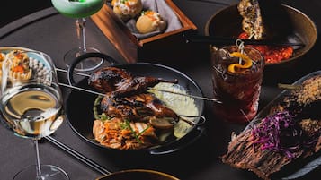 Variedad de platos que incluyen carnes a la parrilla, una ensalada en un tazón y un vaso de bebida roja, sugiriendo un ambiente para comer.