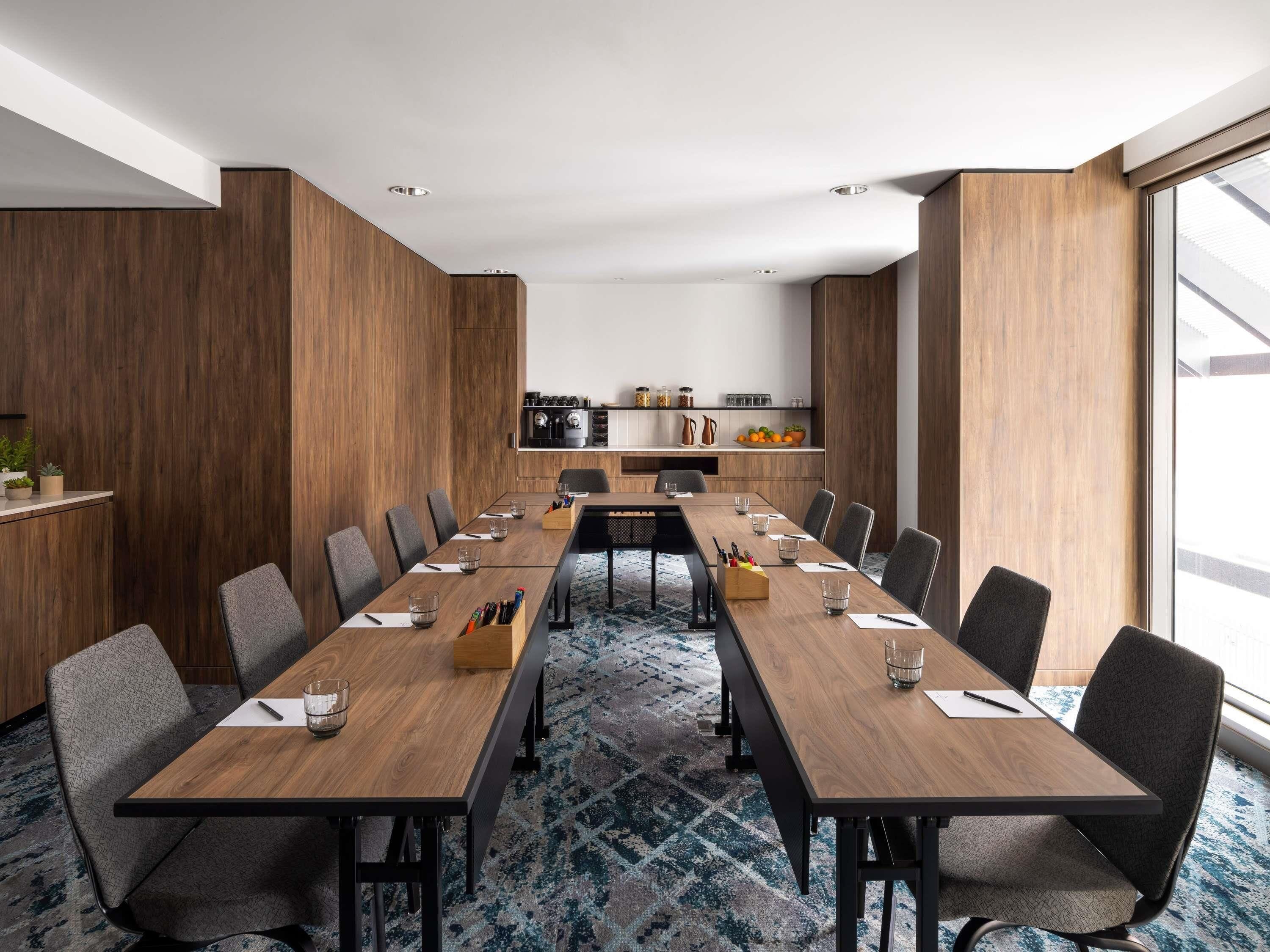 Een vergaderruimte met een lange tafel, stoelen en een keuken op de achtergrond.