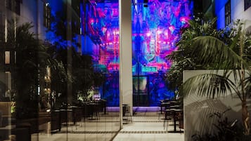A modern indoor space with a central column, seating areas, and a vibrant light display on the back wall.