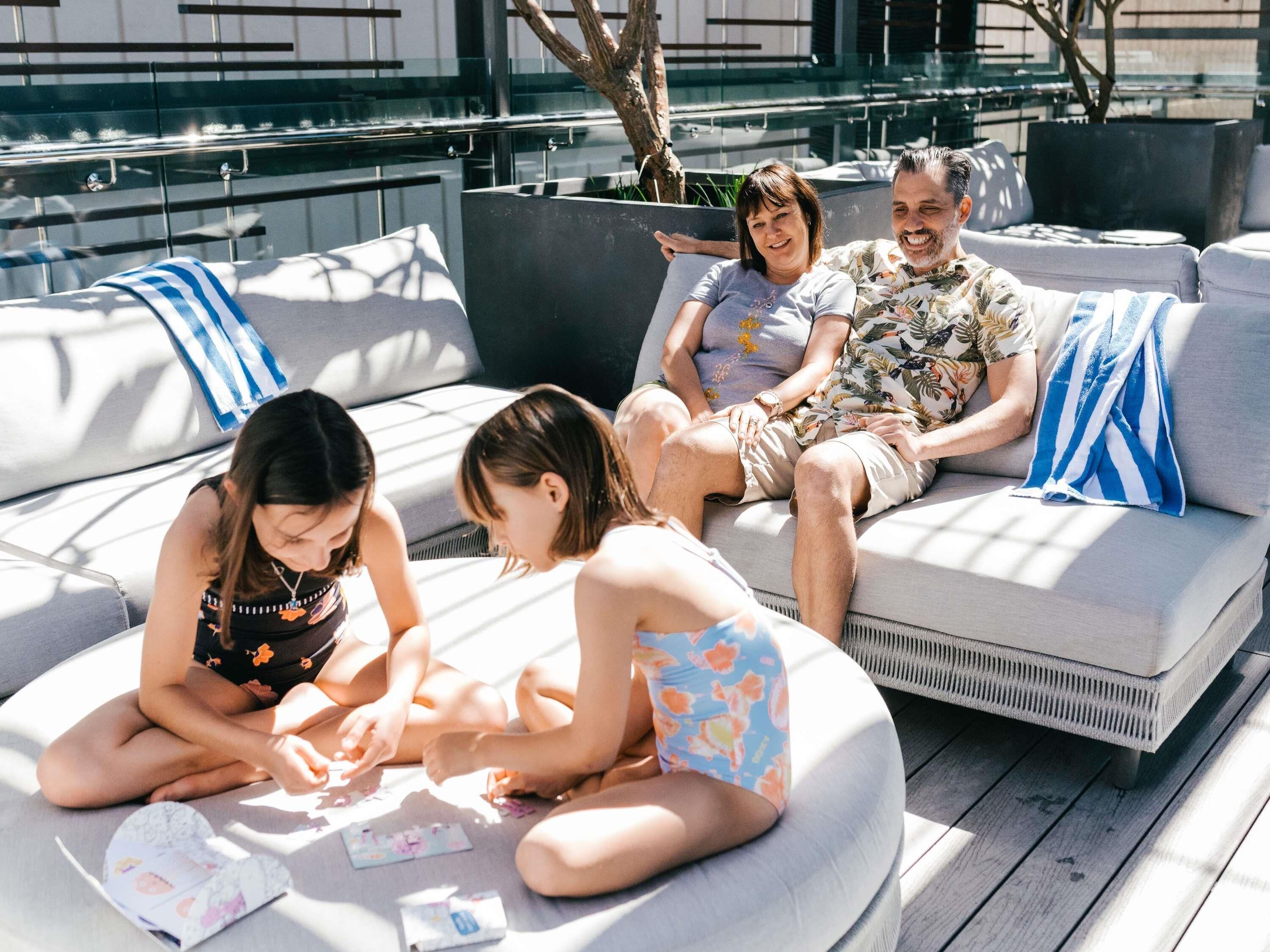 Un grupo de personas sentadas en un área de lounge moderna al aire libre, con una piscina al fondo.
