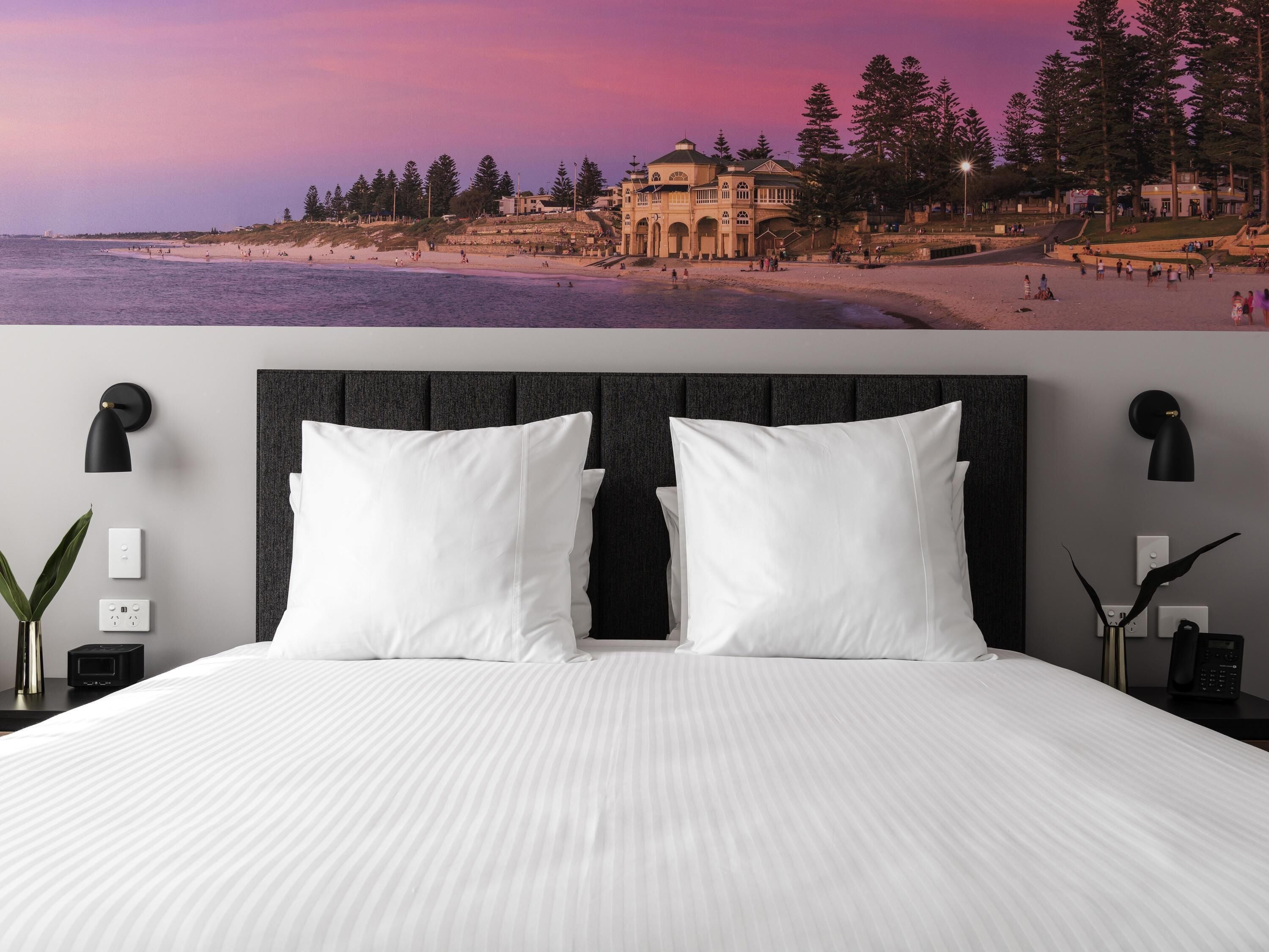 A bed with white linens, a dark headboard, and two bedside lamps.