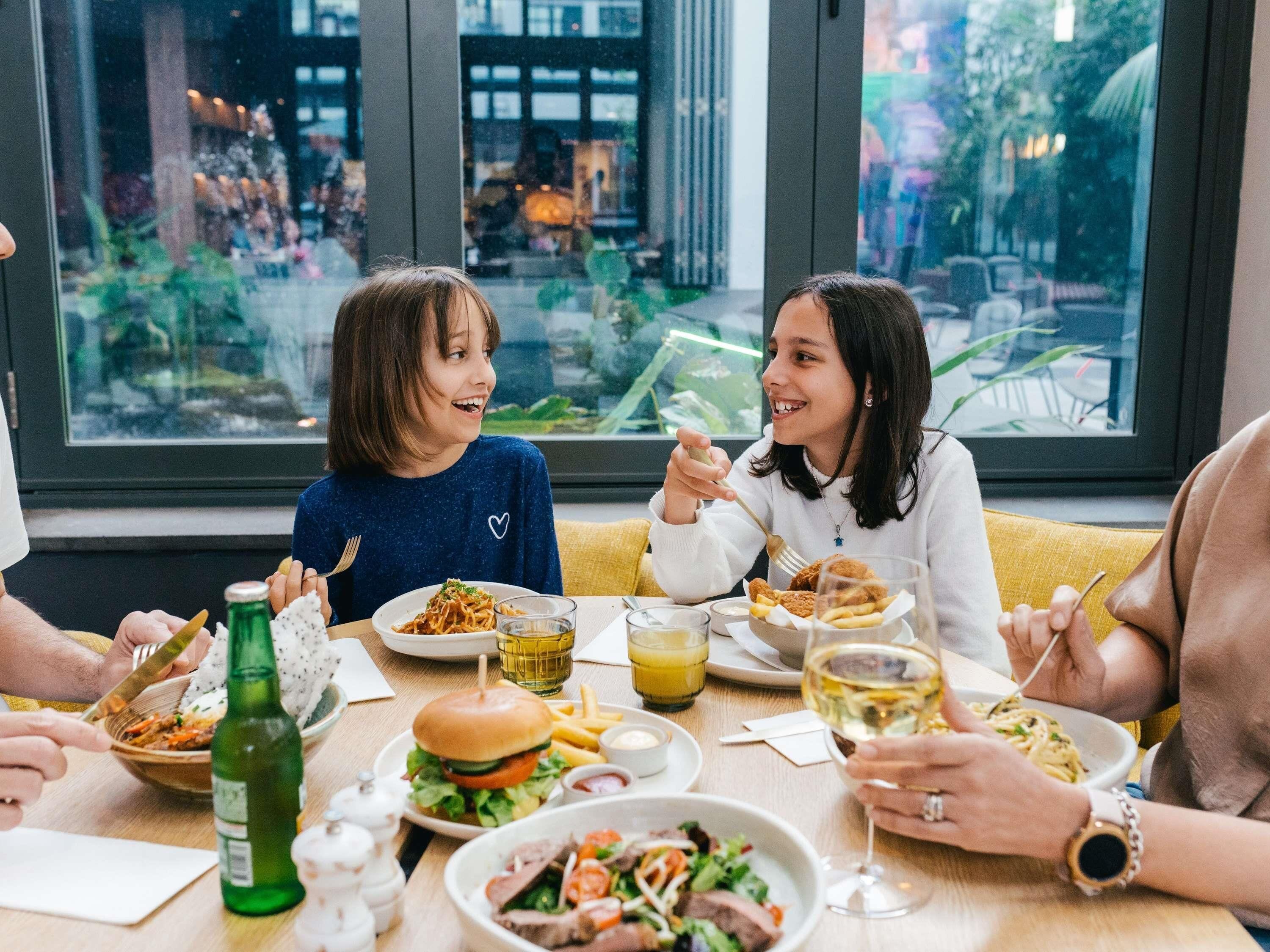 Un groupe de personnes est réuni dans un restaurant, et les grandes fenêtres offrent une vue sur le paysage urbain.