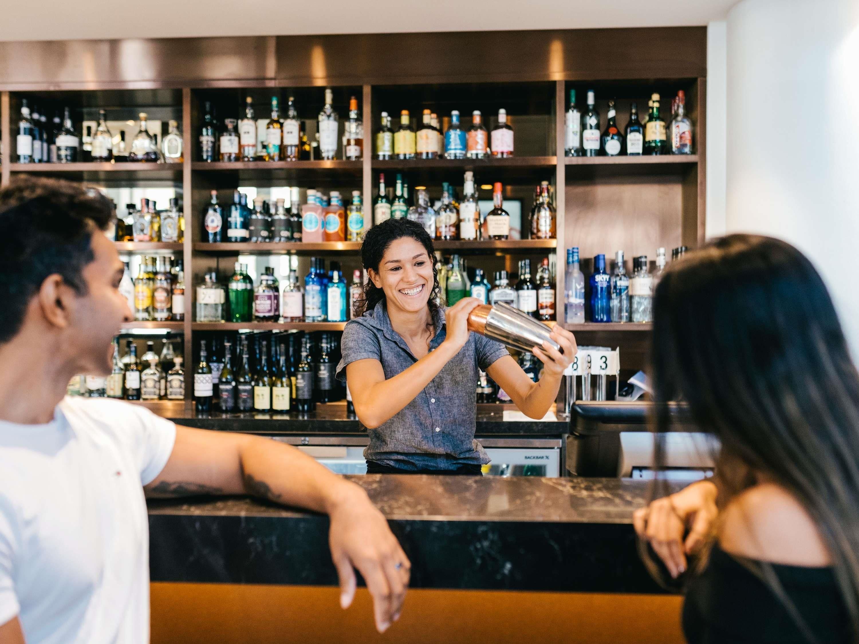 Ein Barkeeper hinter einer Bar mit Regalen voller Spirituosenflaschen.