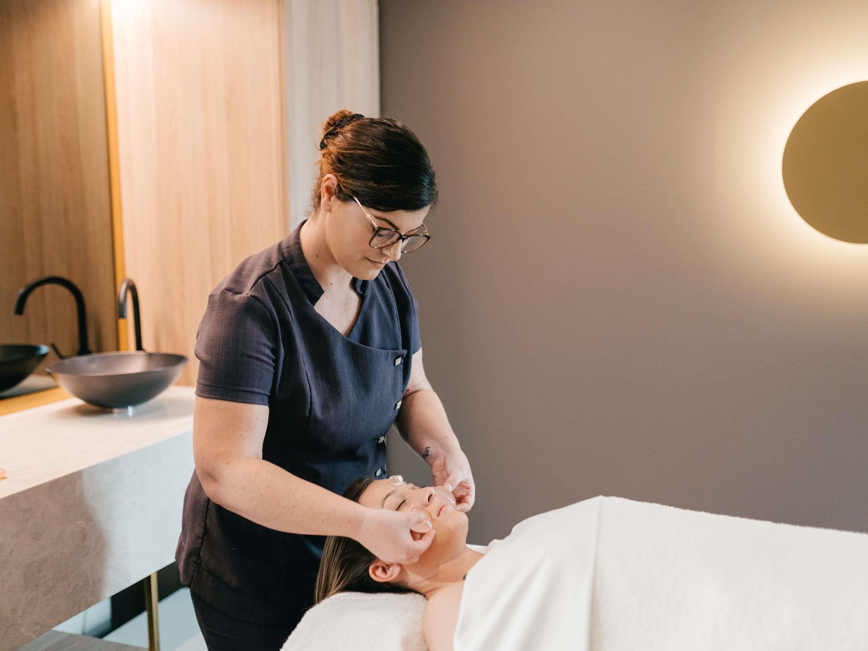 A person receiving a facial treatment in a room with a modern design, a sink, and a mirror.