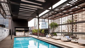 A modern indoor pool area with a clear view of the city skyline, a bar area, and comfortable seating.