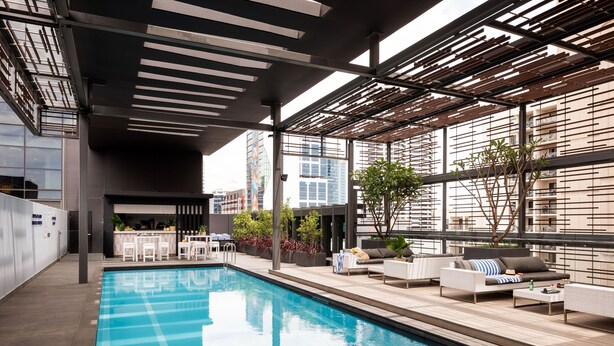 A modern indoor pool area with a clear view of the city skyline, a bar area, and comfortable seating. - Novotel Perth Murray Street (Perth)