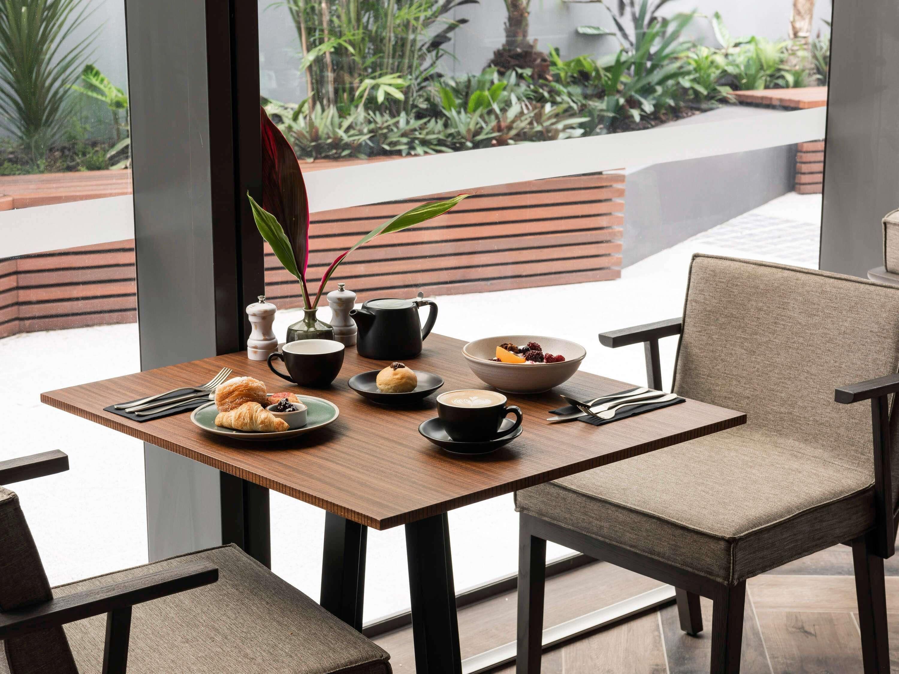 A dining table with a bowl of fruit, a cup of coffee, and pastries.