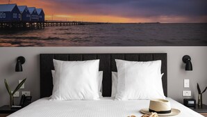 A hotel room with a bed, white bedding, a hat, a clock, and a wall-mounted lamp.