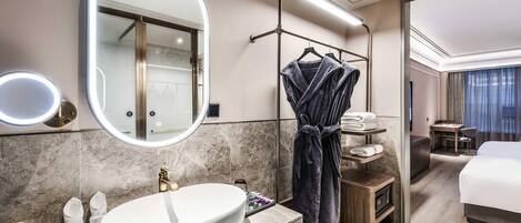 A modern hotel bathroom with a large mirror, a sink, and a robe rack.