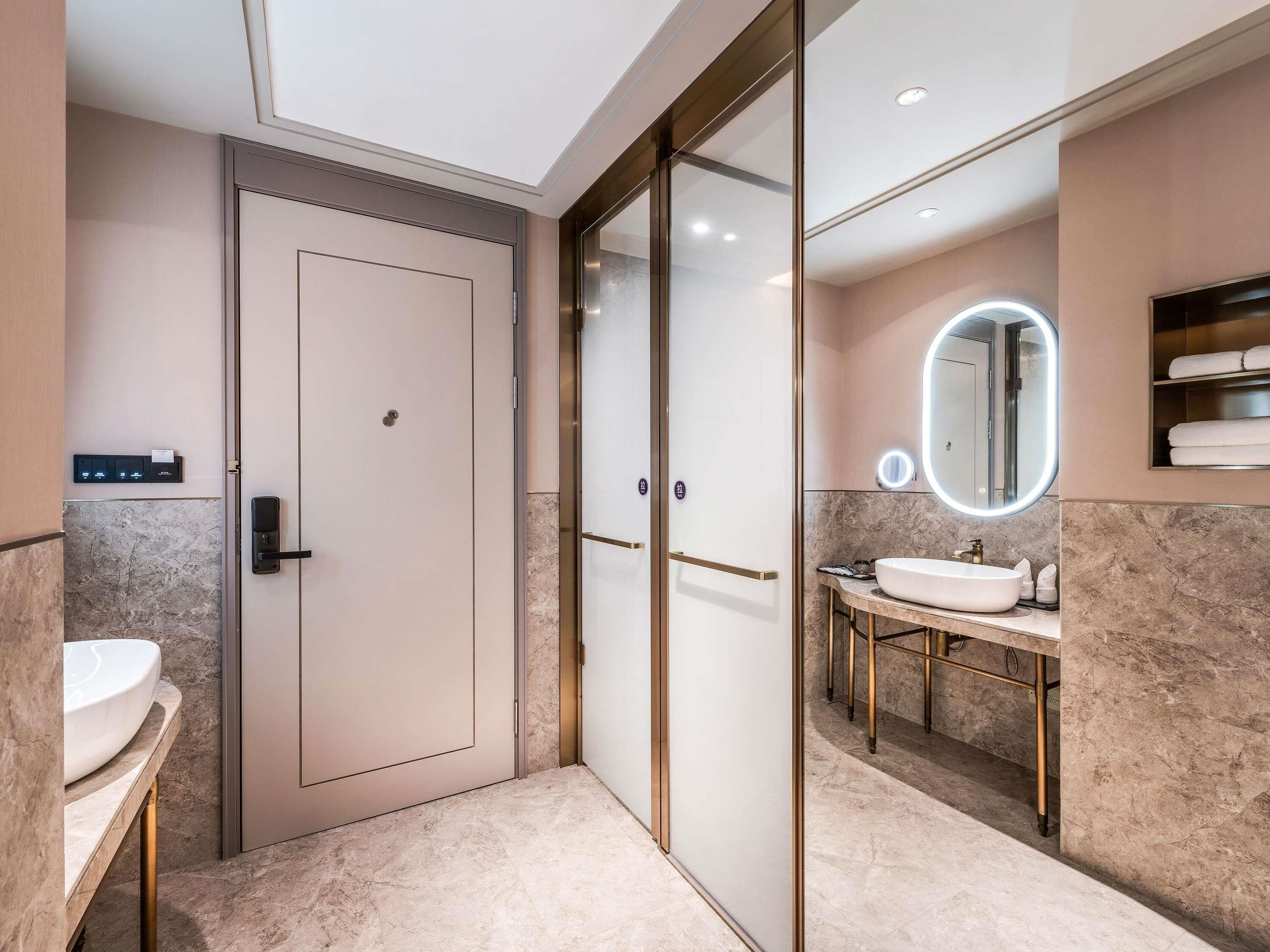 A modern bathroom with a glass door, a vanity with a sink, and a mirror with a light.