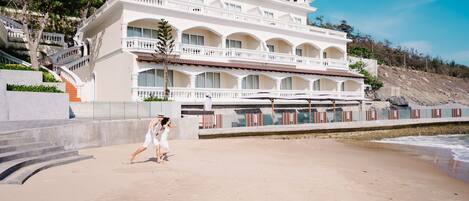 Un hotel grande de varios pisos con fachada blanca, balcones y vistas a la playa.