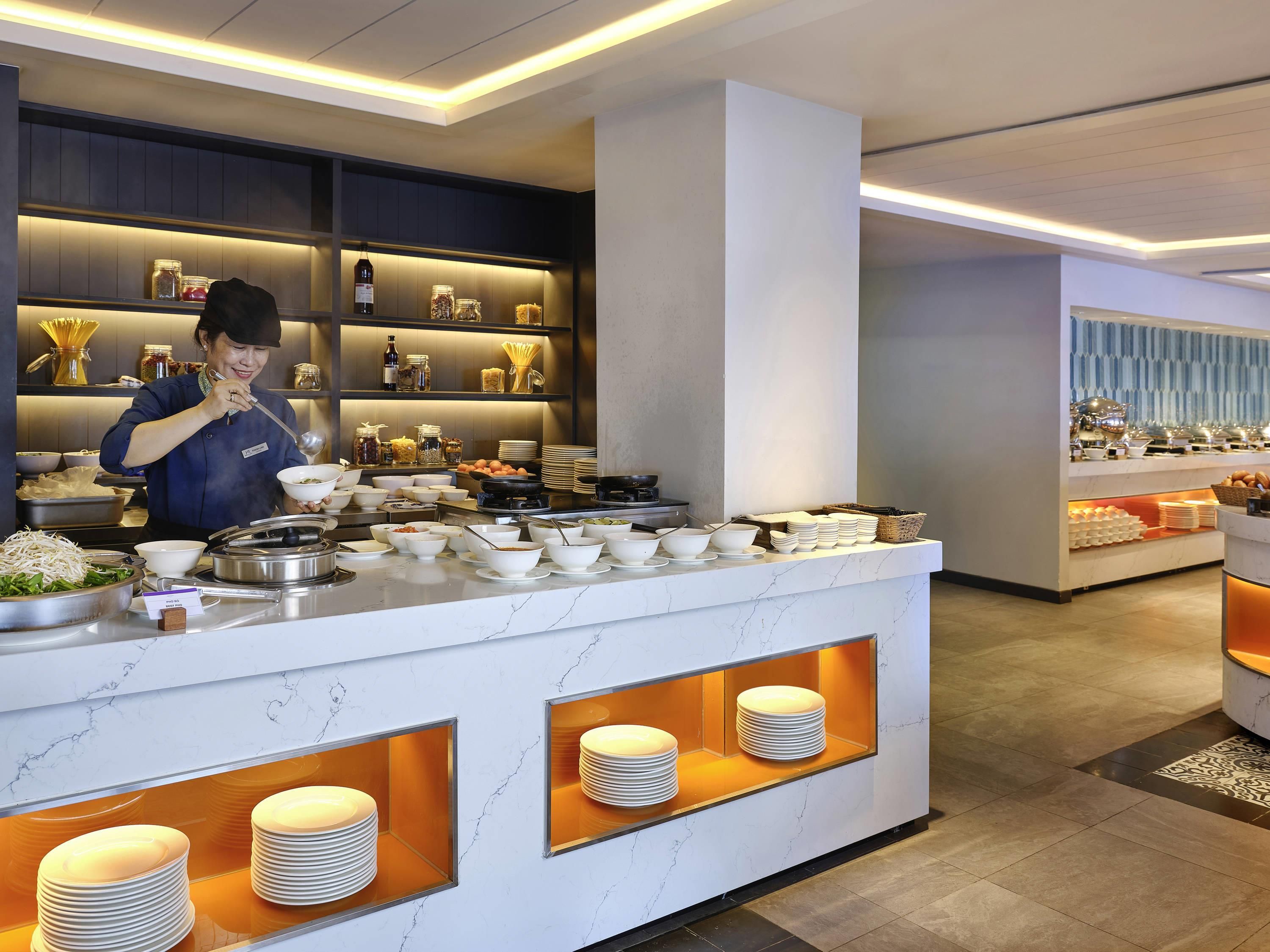 A buffet setup with a variety of food items and utensils, a staff member serving, and neatly arranged plates and bowls.