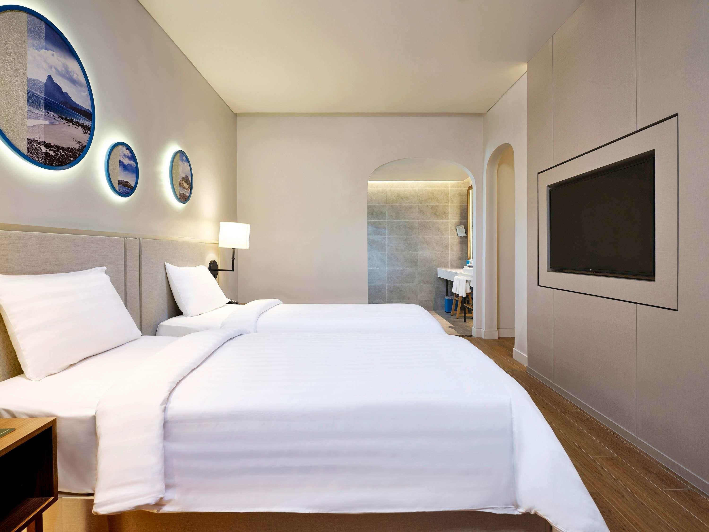 A hotel room with a large bed, a TV mounted on the wall, and a bathroom visible through an archway.