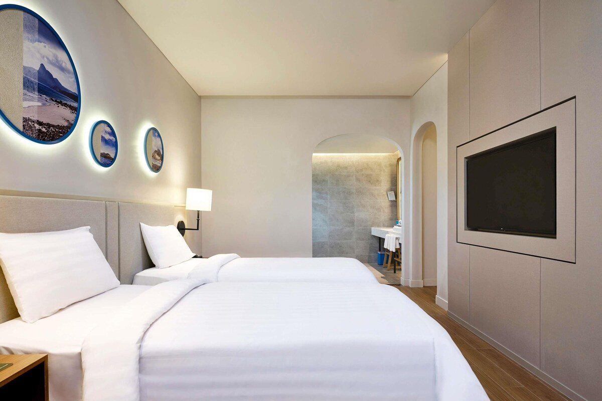 A hotel room with a large bed, a TV mounted on the wall, and a bathroom visible through an archway.