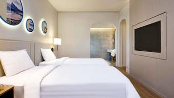 A hotel room with a large bed, a TV mounted on the wall, and a bathroom visible through an archway.