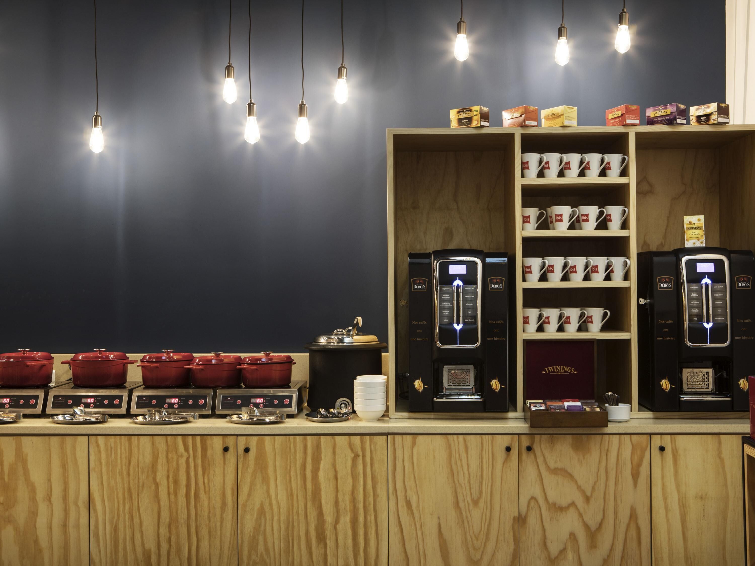 Una cafetería con varias máquinas de café, una exhibición de tazas y un mostrador con recipientes rojos.