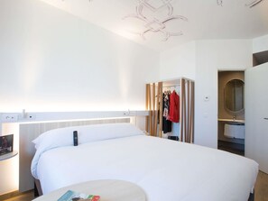 Habitación de hotel con una cama grande, una mesita de noche, un armario y un baño con espejo.